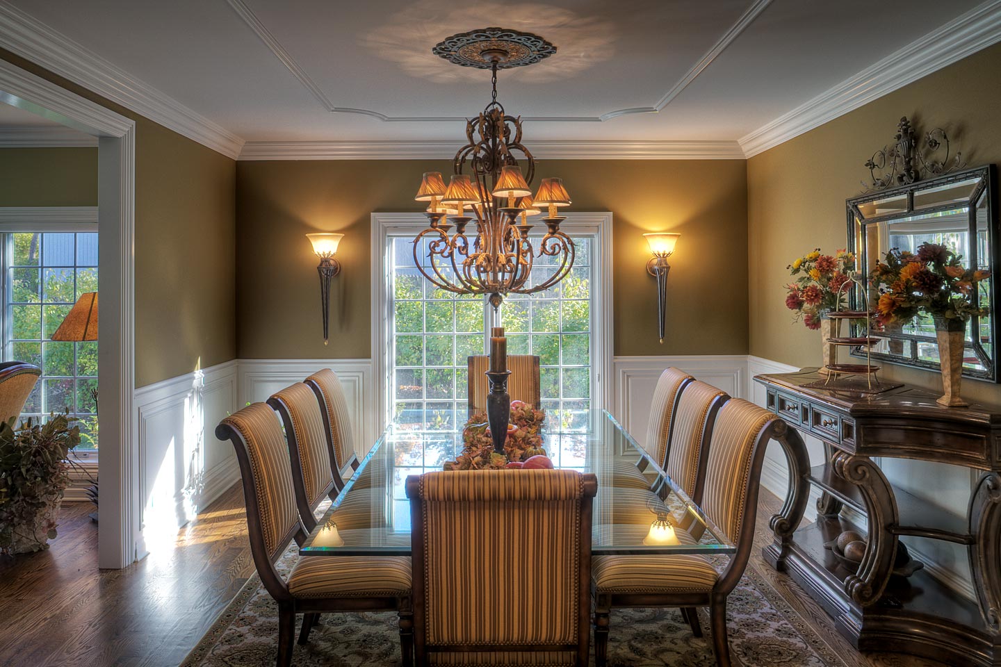 a beautifully decorated formal dining room featuring wainscoting and a long glass dining room table, photographed by Jacob Rosenfeld