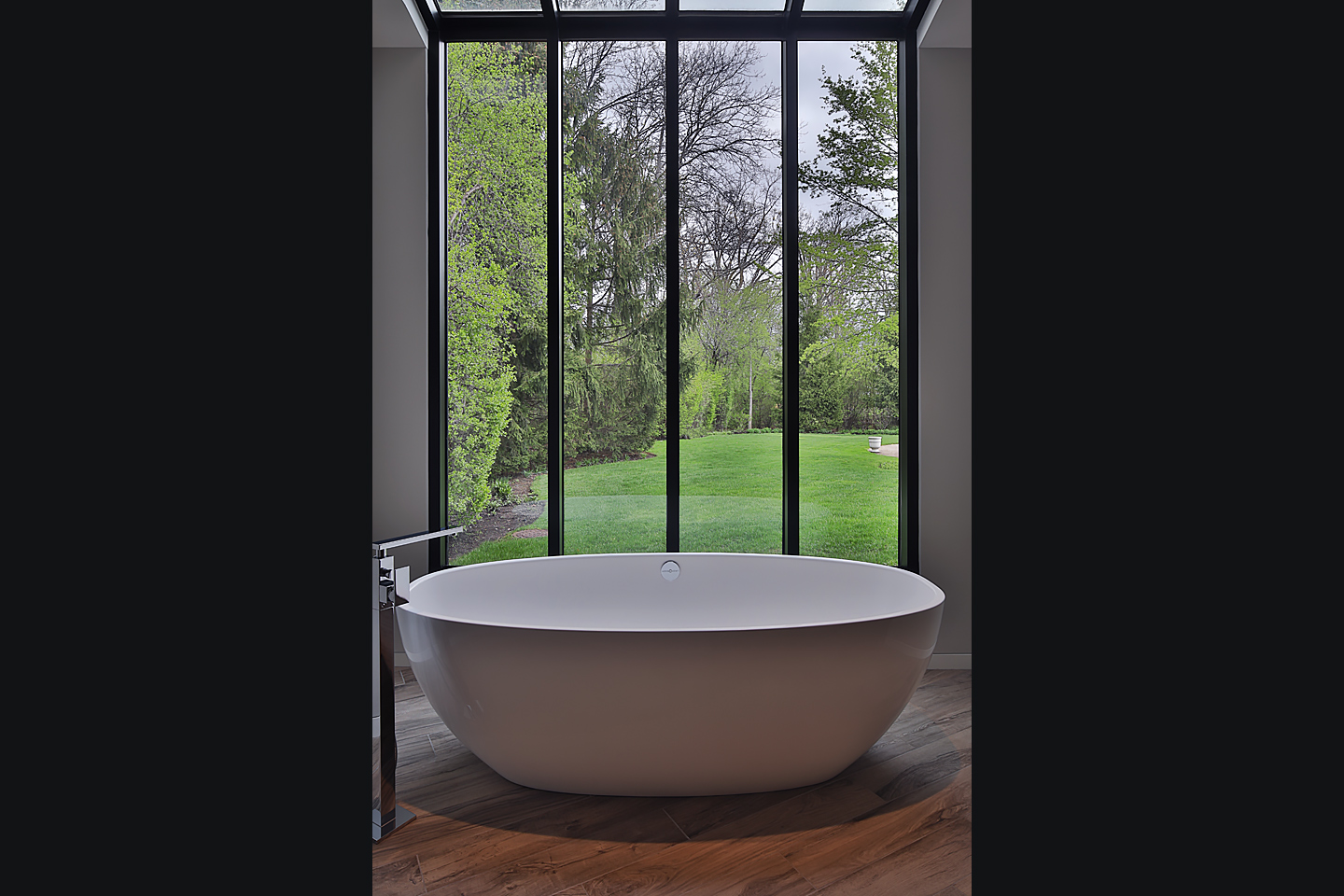 a modern master bath, freestanding tub sitting beside a large bank of windows, photographed by Jacob Rosenfeld